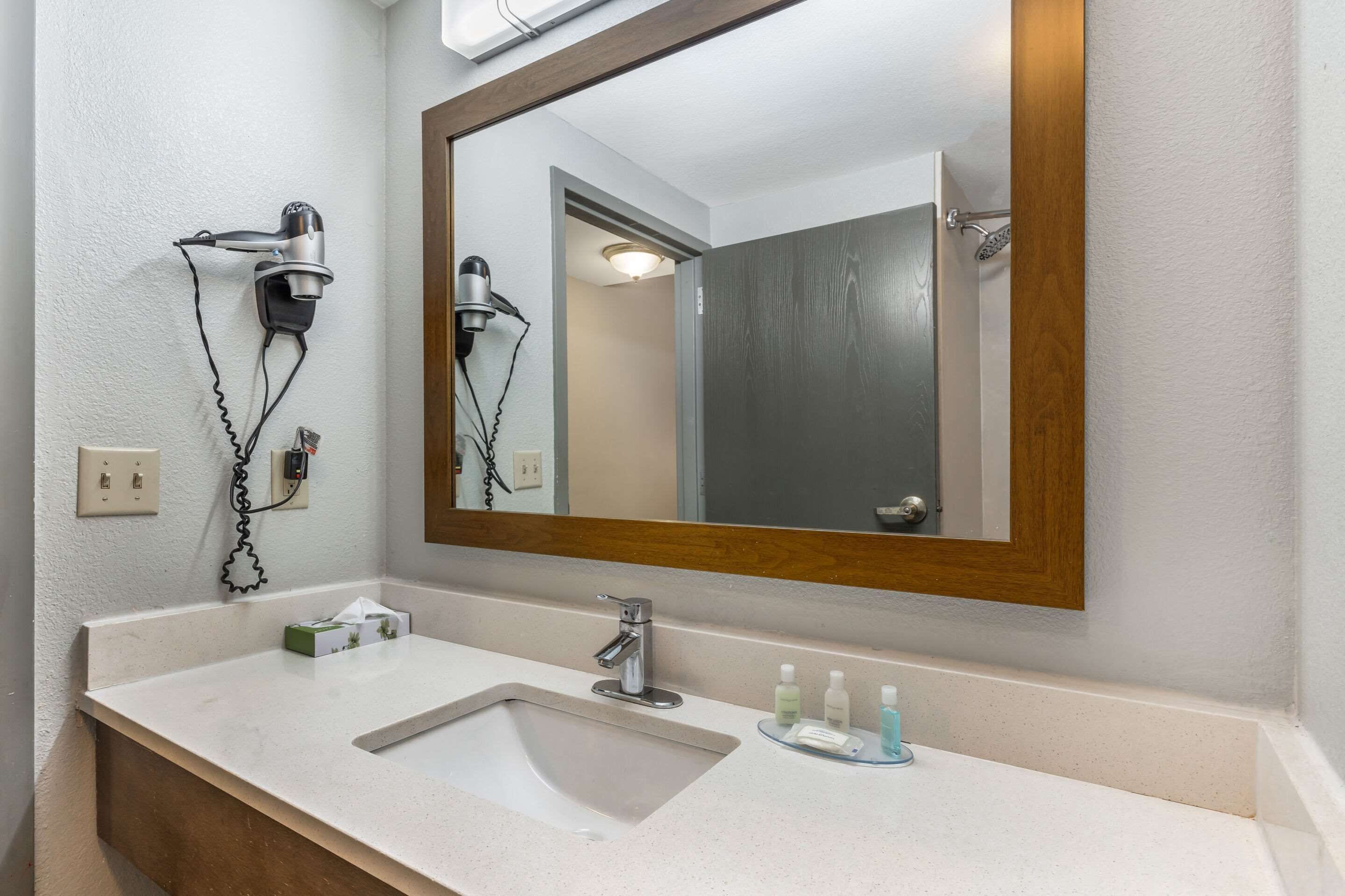 A bathroom with a sink, mirror, and hair dryer mounted on the wall.