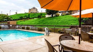 A swimming pool with a patio area, outdoor seating, and a view of a hill with a building in the background. - Clarion Inn near Lookout Mountain (Chattanooga)
