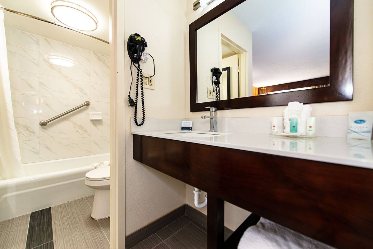 A bathroom with a bathtub, toilet, vanity, and a hairdryer on the wall.