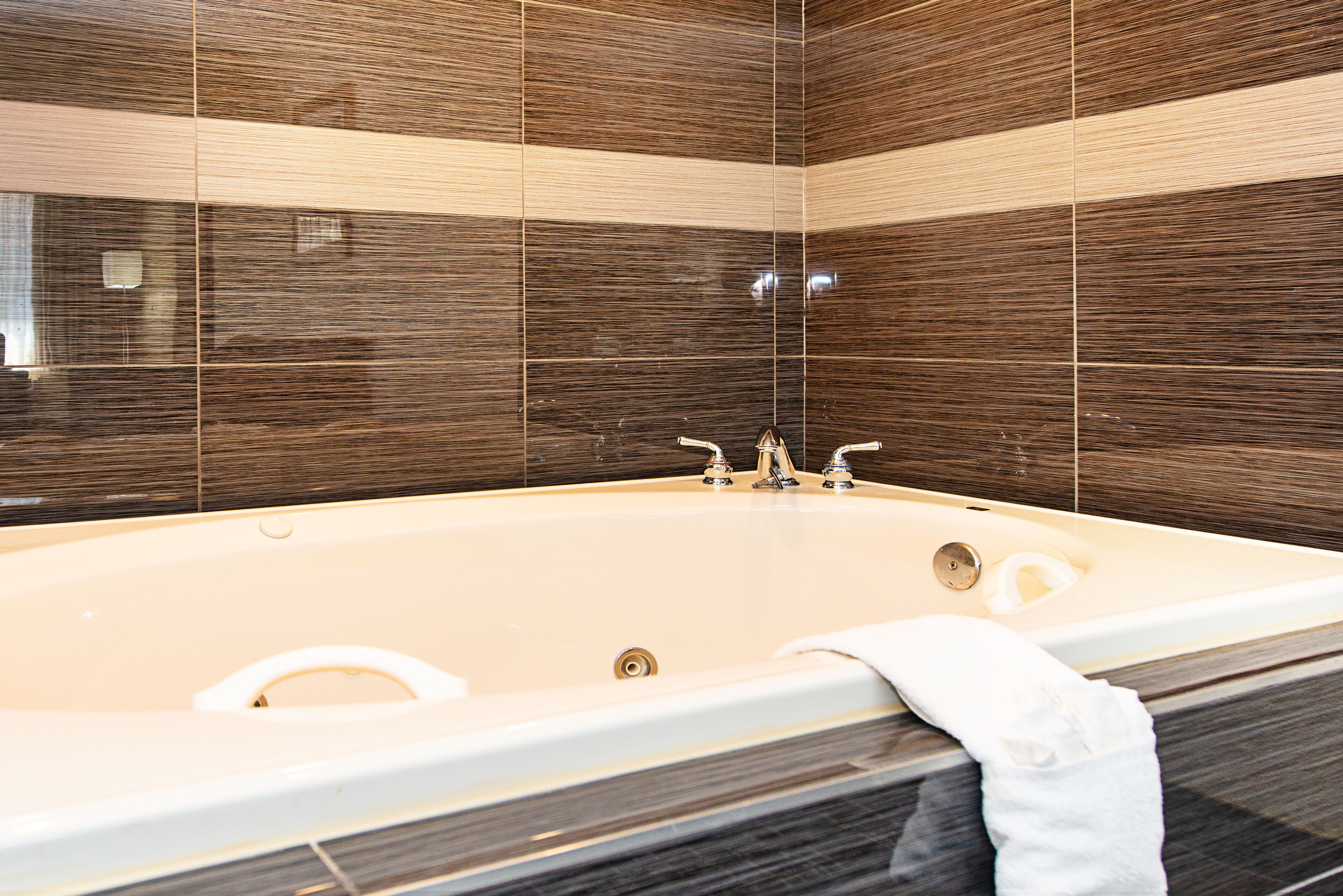 A modern bathroom with a large bathtub, a mirror, and dark patterned tiles.