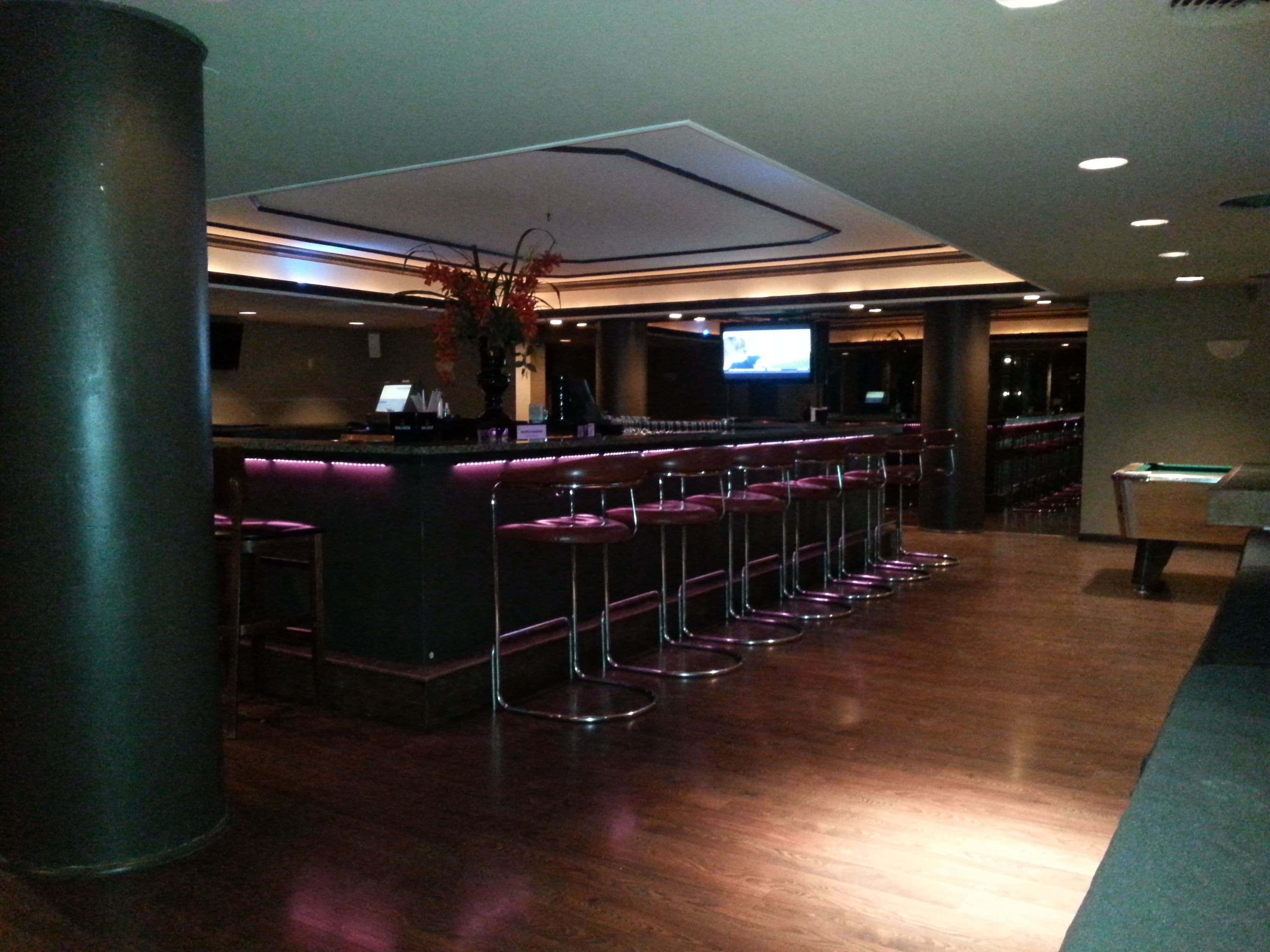 A bar area with a long counter, multiple stools, and a television screen.