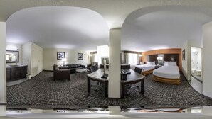Habitación de hotel con una cama grande, un escritorio, una silla, un sofá y un baño a la vista a través de una puerta abierta.