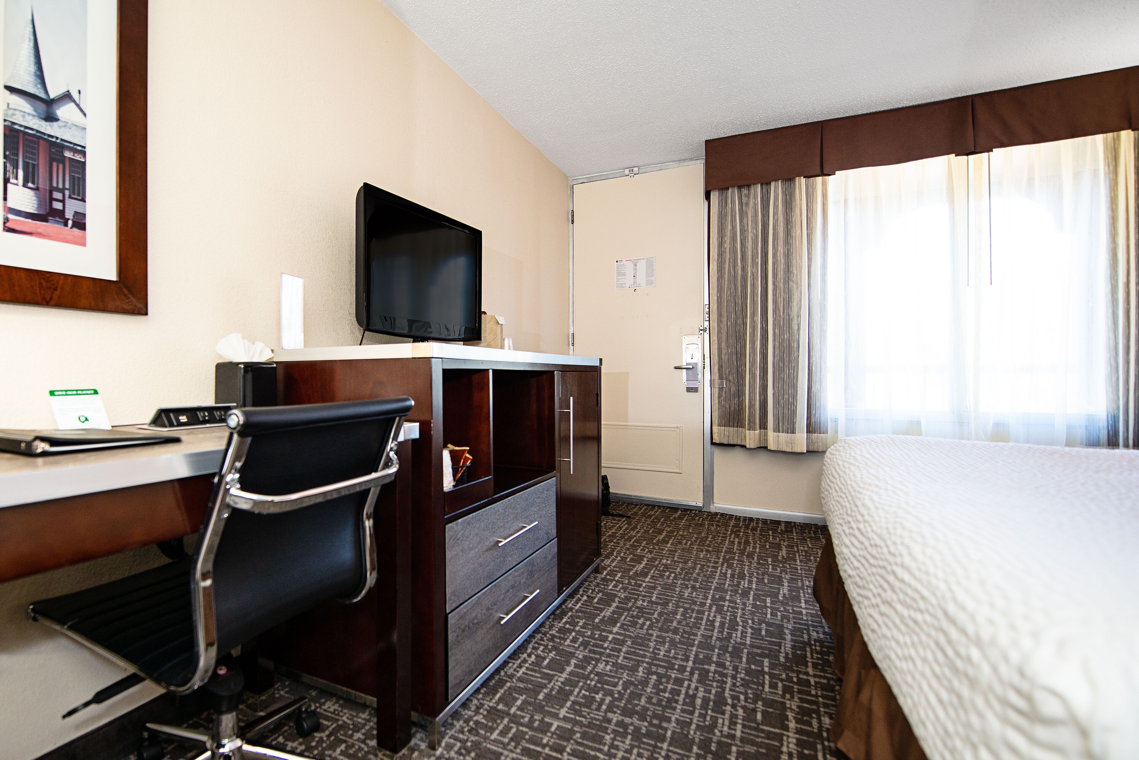 Een hotelkamer met een bed, een bureau met stoel, een televisie en een raam met gordijnen.