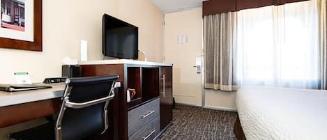 A hotel room with a bed, a desk with a chair, a television, and a window with curtains.
