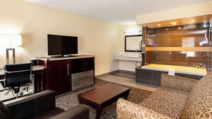 Una habitación de hotel moderna con televisor de pantalla plana, un sofá, una mesita de centro, un escritorio con una silla, un tocador con espejo y una bañera.