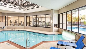 Una piscina interior con equipamiento de ejercicio, ventanas amplias y vistas a una piscina exterior.