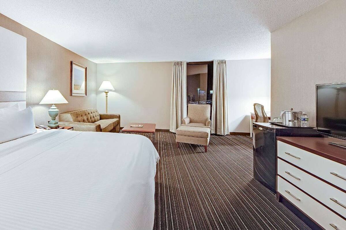 A hotel room with a large bed, a desk with a TV, a chair, and a sofa.