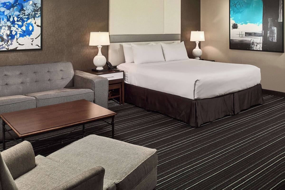 A hotel room with a bed, a sofa, a small table, and two nightstands with lamps.
