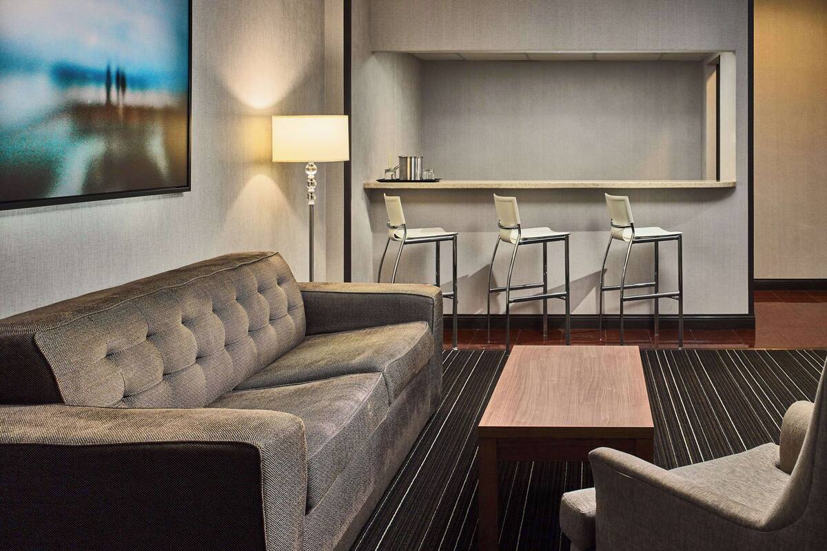 A hotel room with a sofa, a small table, and three bar stools.