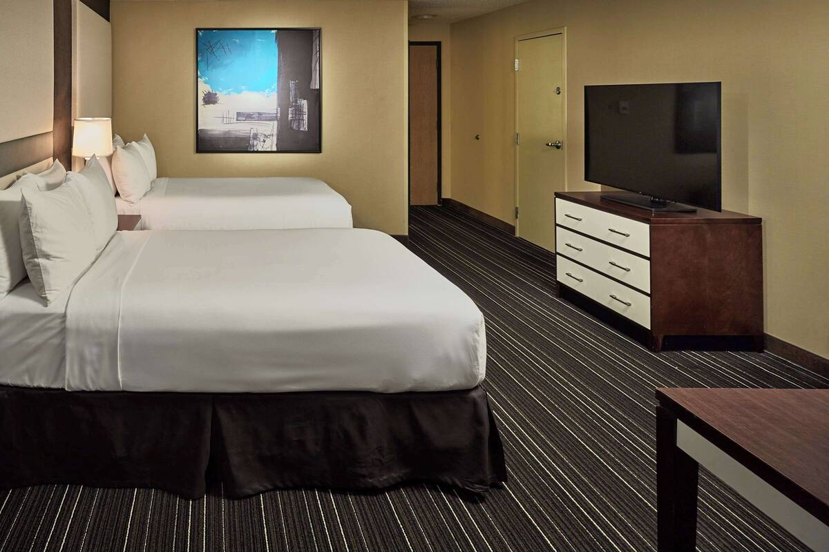 A hotel room with two beds, a flat-screen TV, a dresser, and a painting on the wall.