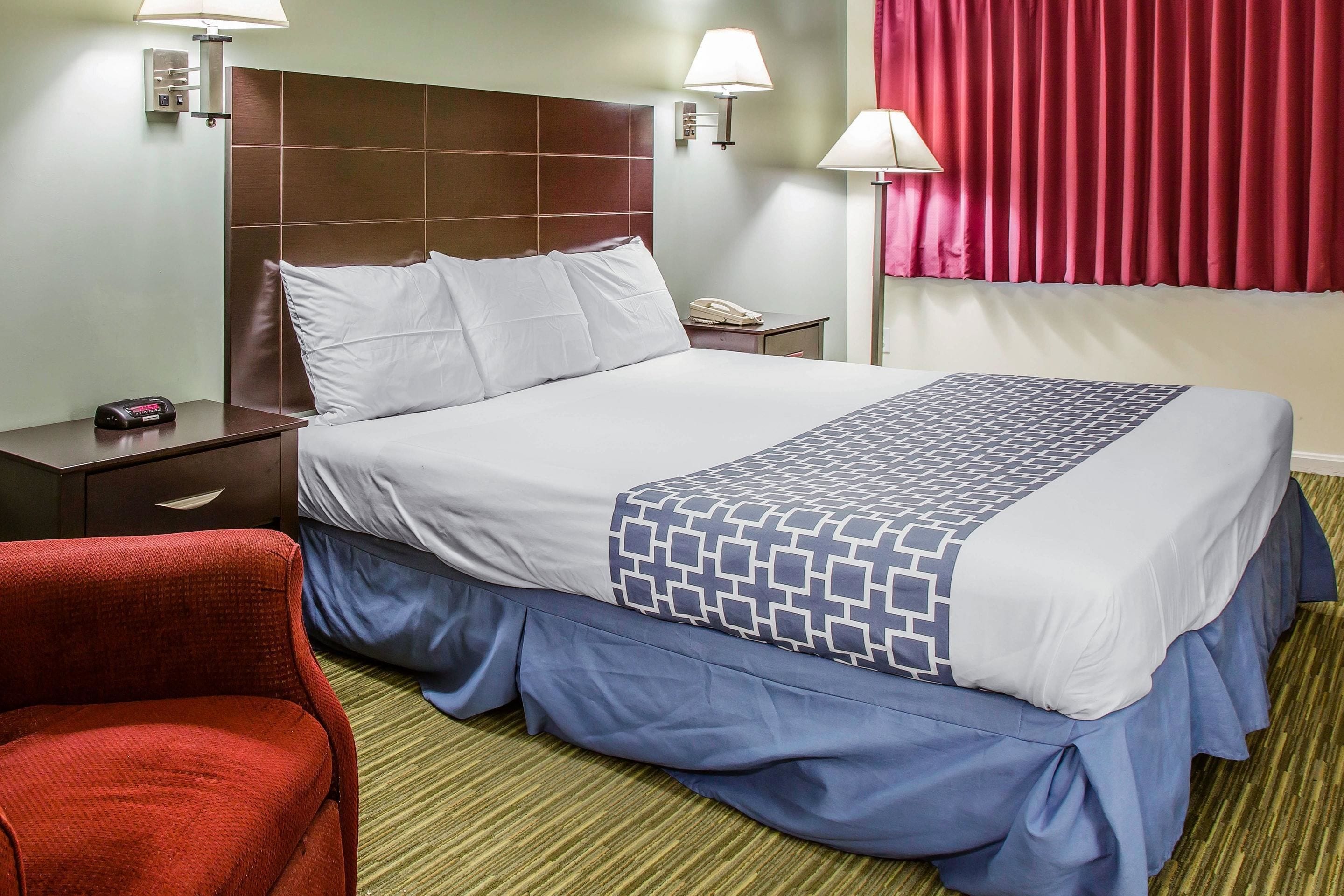 A hotel room with a large bed, a nightstand, a red chair, and a telephone.