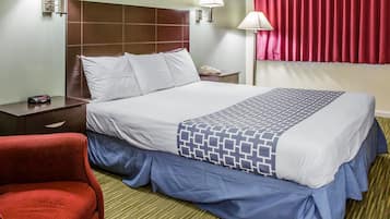 A hotel room with a large bed, a nightstand, a red chair, and a telephone.