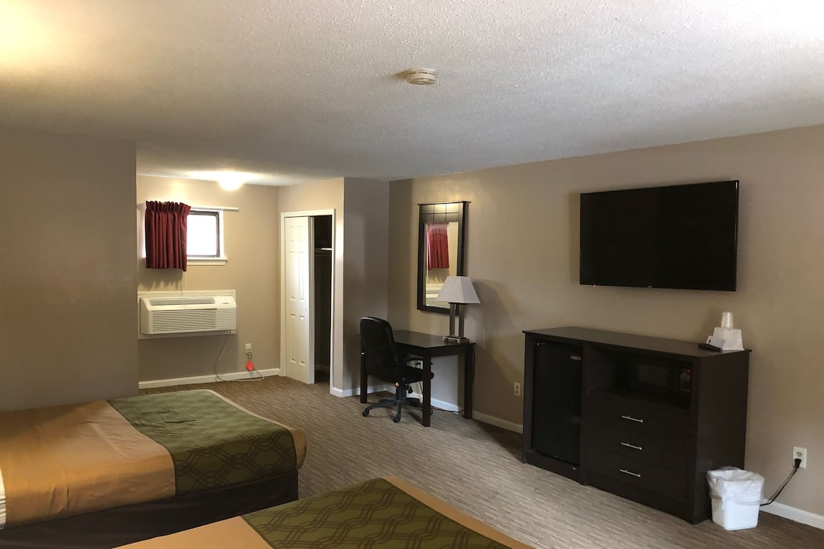 Una habitación de hotel con cama, escritorio, silla, televisor y un pequeño cubo de basura.