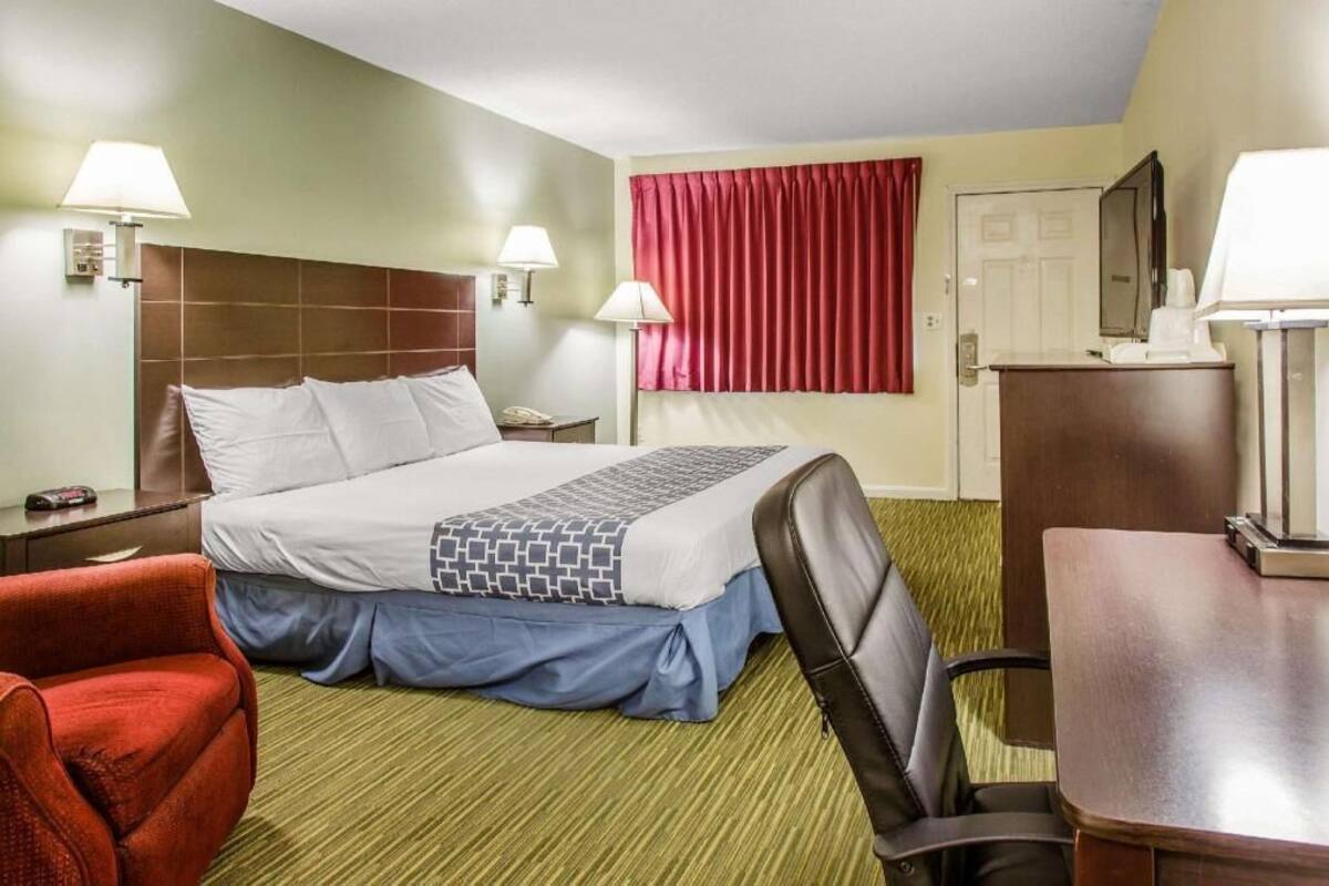 Habitación de hotel con cama, dos lámparas de noche, un escritorio, una silla, una cortina roja y una puerta.