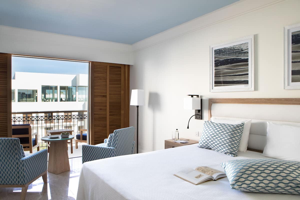 Habitación de hotel con una cama grande, un balcón con asientos y dos cuadros en la pared.