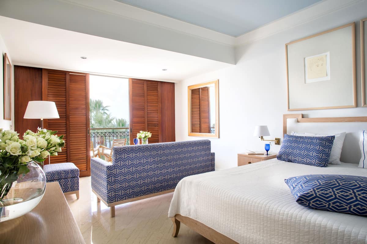 Una habitación de hotel con cama, sofá, mesita de noche y ventana con contraventanas de madera.