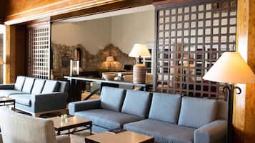 Ein stilvoller Lounge-Bereich mit Steinwand, blauen Sofas, Holztischen und einem dekorativen Raumteiler.