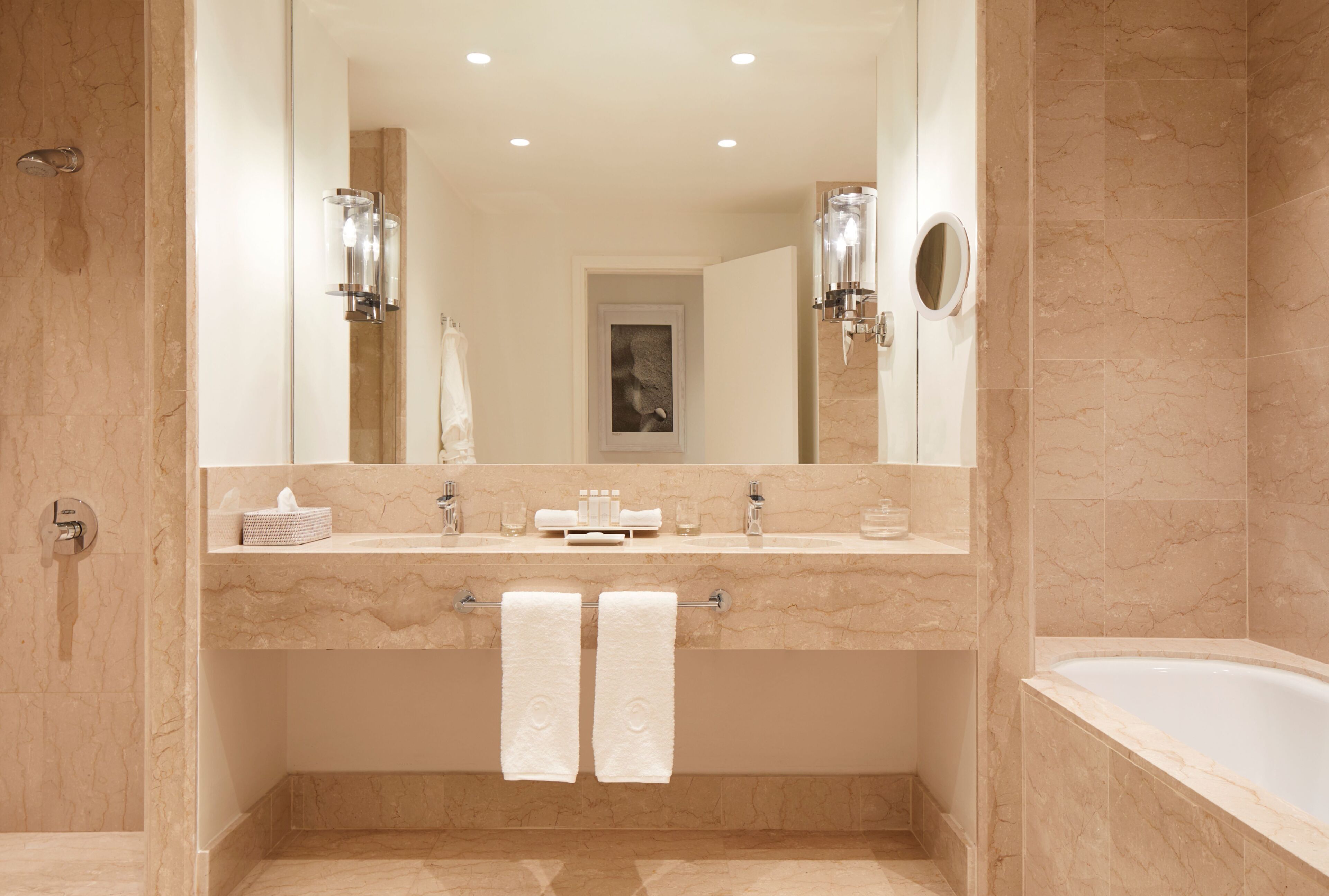 A modern bathroom with a large mirror, two sinks, a bathtub, and a towel rack with two towels.