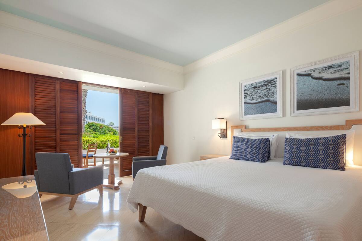 Habitación de hotel con una cama grande, dos sillas, una mesita y vistas a zonas verdes.