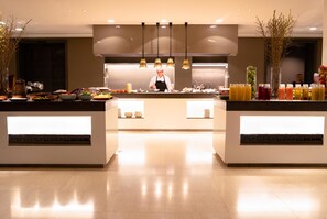 A modern kitchen with a chef preparing food, a buffet with various dishes, and a clean, well-lit environment.