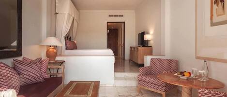 A hotel room with a bed, a sofa, a chair, a small table, a lamp, and a TV.