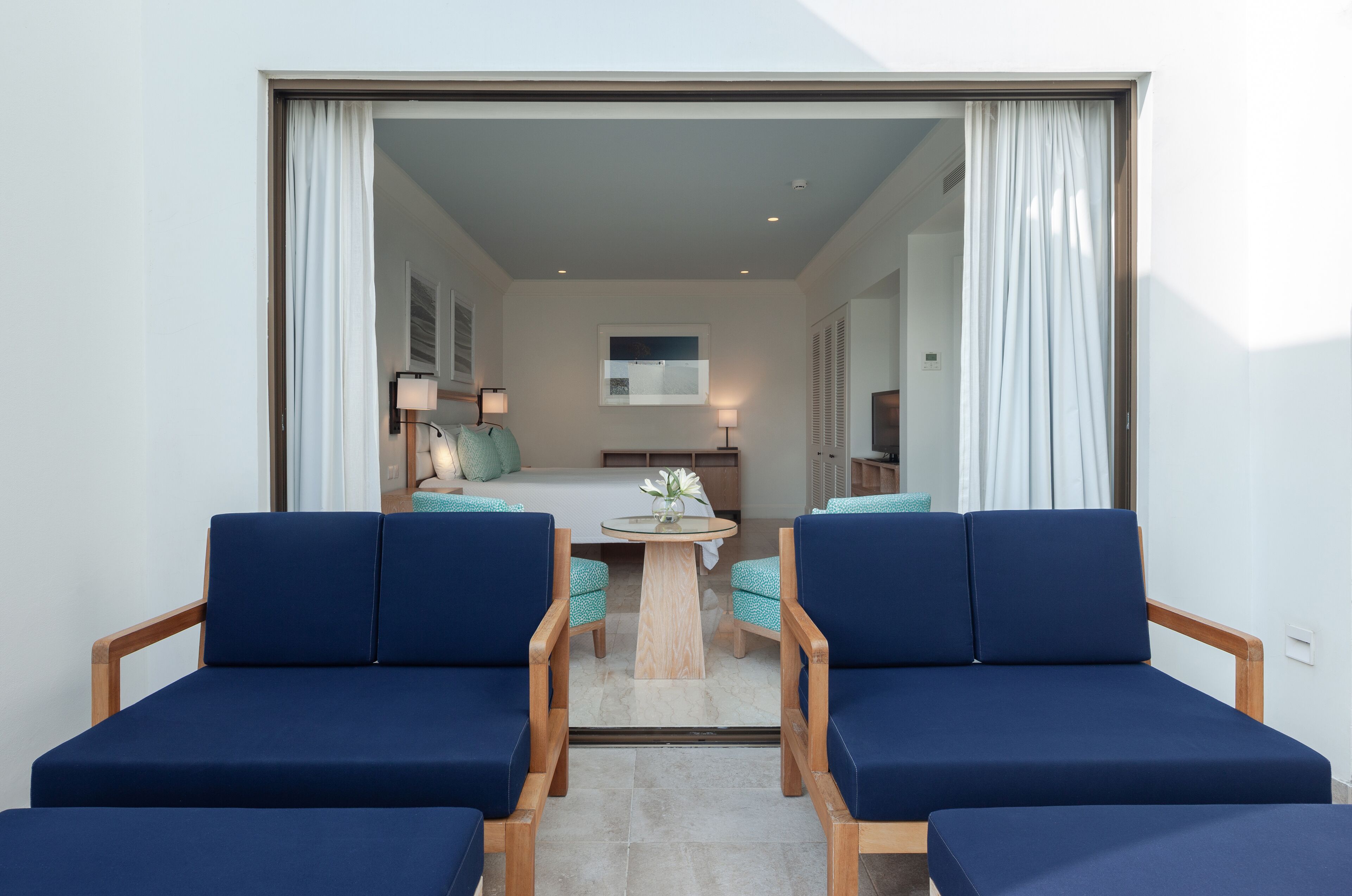 A modern room with two blue sofas, a small round table, and a bed in the background.