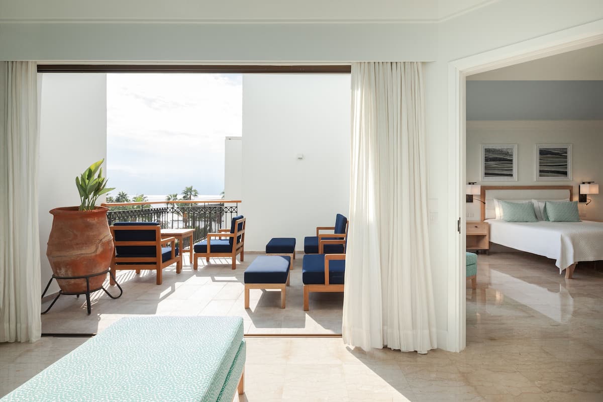 Habitación de hotel con balcón, cama, escritorio y zona de estar con sillas y mesa.