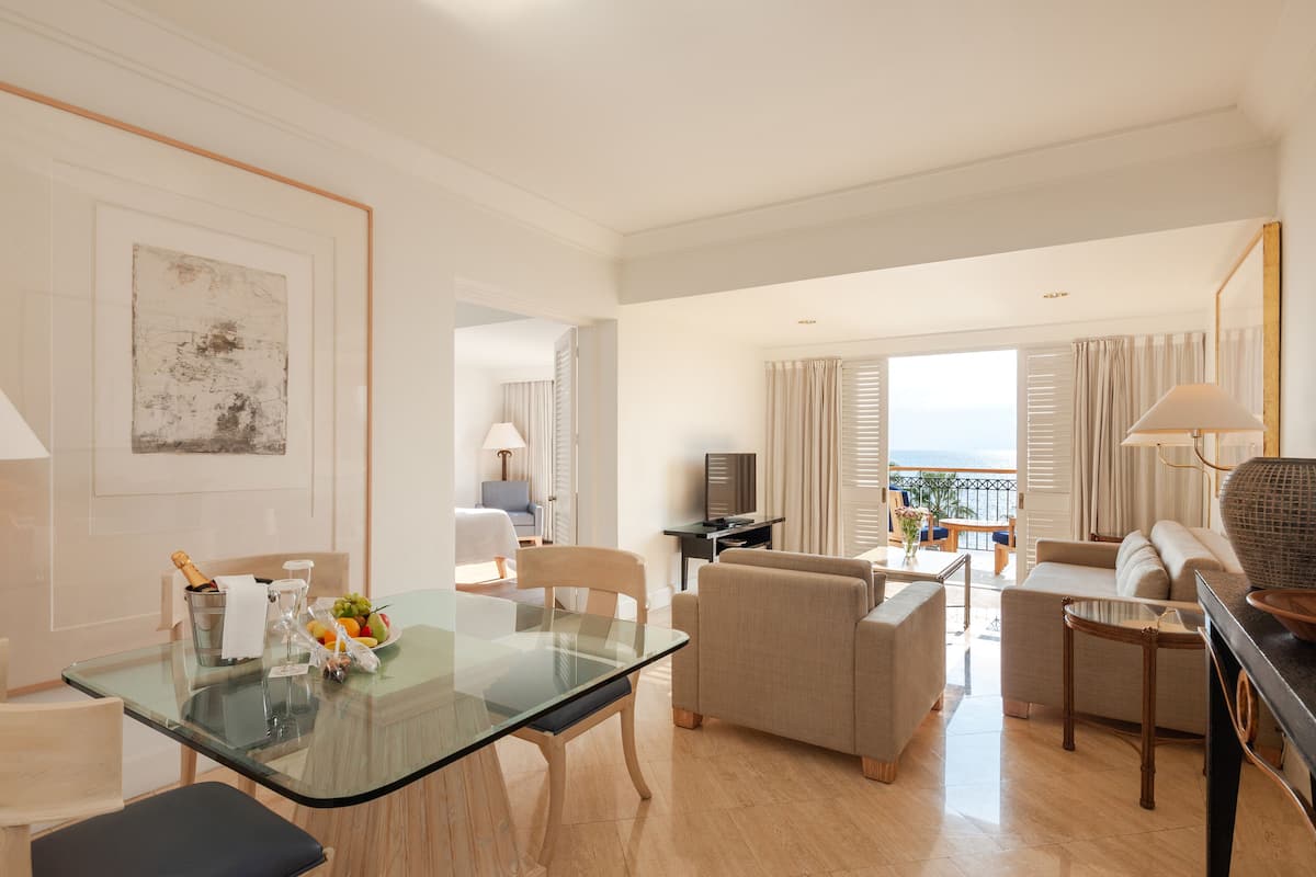 Una sala de estar moderna con una mesa de comedor de cristal, sofás color beige y vista al mar.