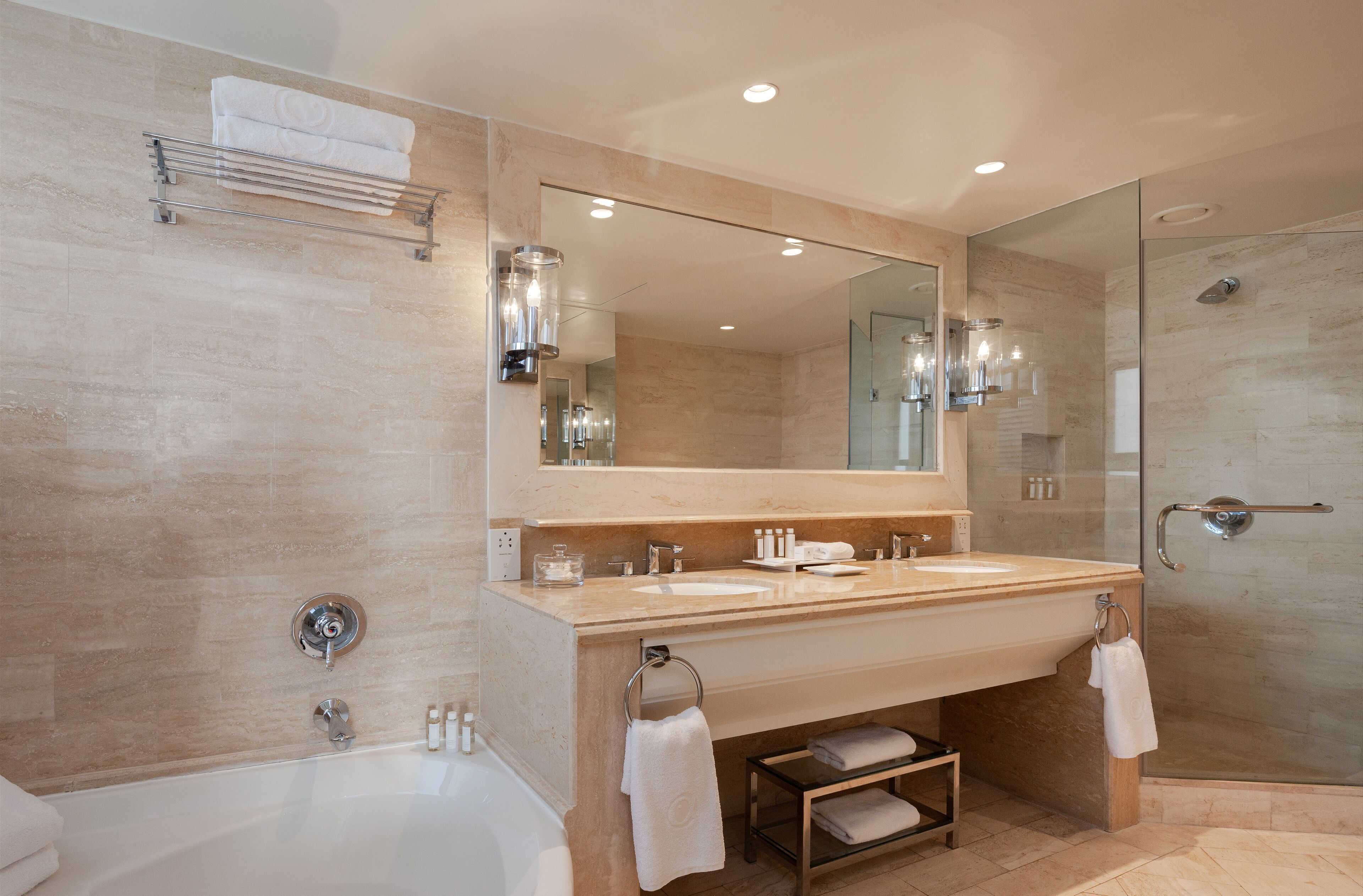 A modern bathroom with a large mirror, two sinks, a bathtub, and a glass-enclosed shower.