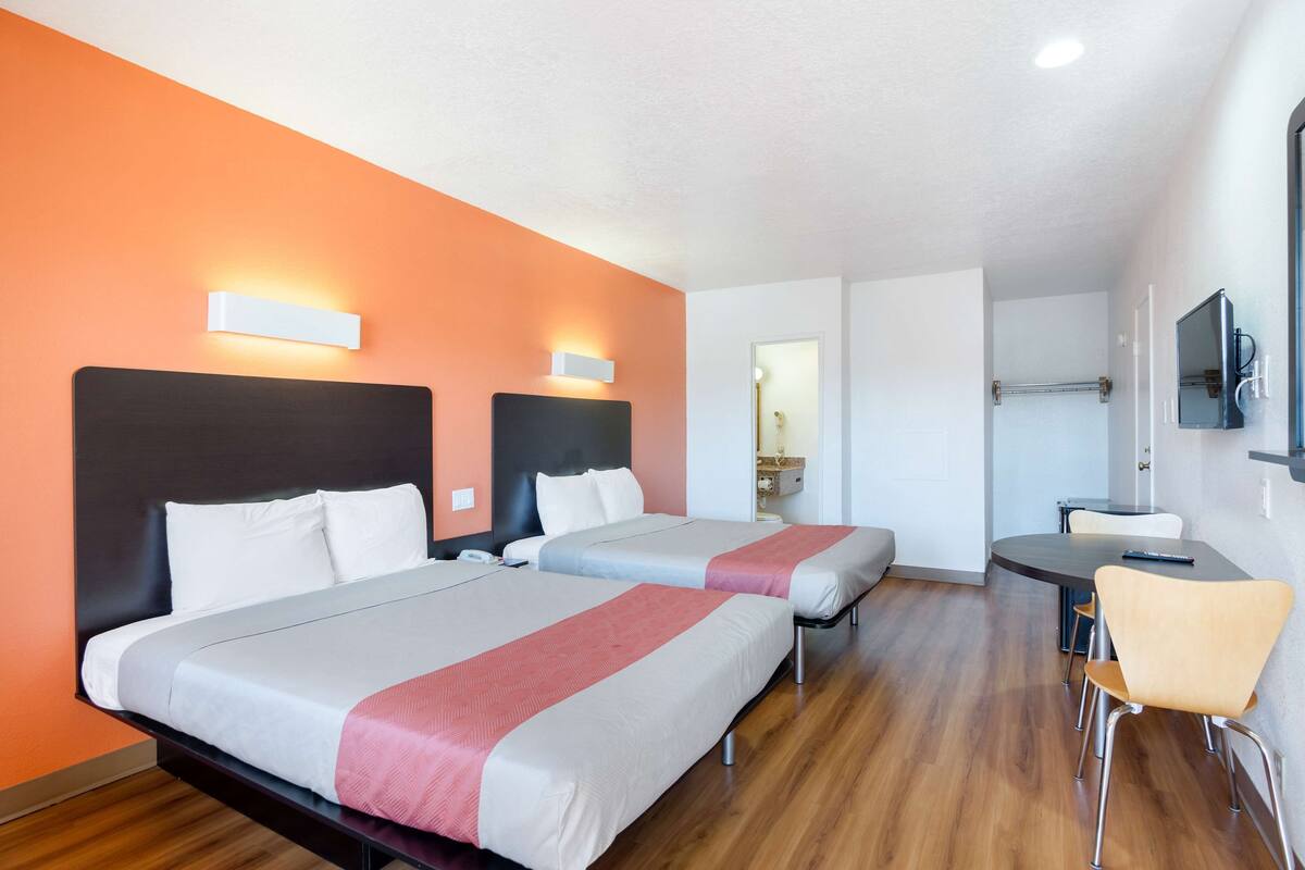 Ein Hotelzimmer mit zwei Betten, einem Schreibtisch, einem Stuhl und einem Fernseher.