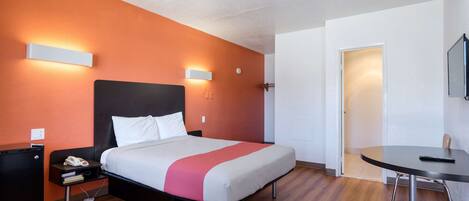Una habitación de hotel con cama, mesita de noche, escritorio, silla y televisor.