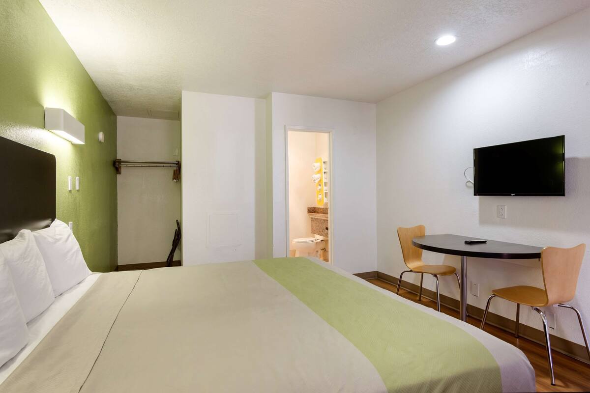 Ein Hotelzimmer mit einem Bett, einem Schreibtisch, zwei Stühlen, einem Fernseher und einem sichtbaren Badezimmer hinter einer offenen Tür.