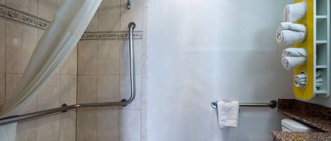 A bathroom with a shower, grab bars, a white toilet, and a towel rack.