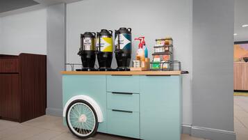 A kitchen area with a teal-colored cabinet featuring a wheel, three coffee dispensers labeled 'HOT WATER,' 'Regular,' and 'Decaf Coffee,' and a bottle of hand sanitizer.