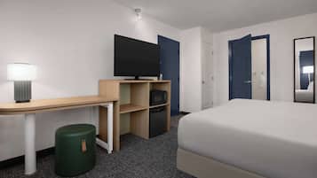 A hotel room with a bed, a desk with a lamp, a television, a microwave, and a trash bin.