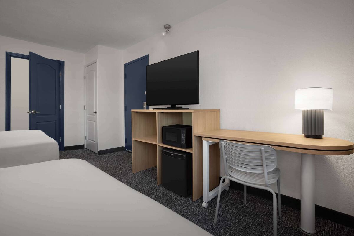 Ein Hotelzimmer mit zwei Betten, einem Schreibtisch mit Lampe, einem Fernseher, einer Mikrowelle und einem kleinen Kühlschrank.