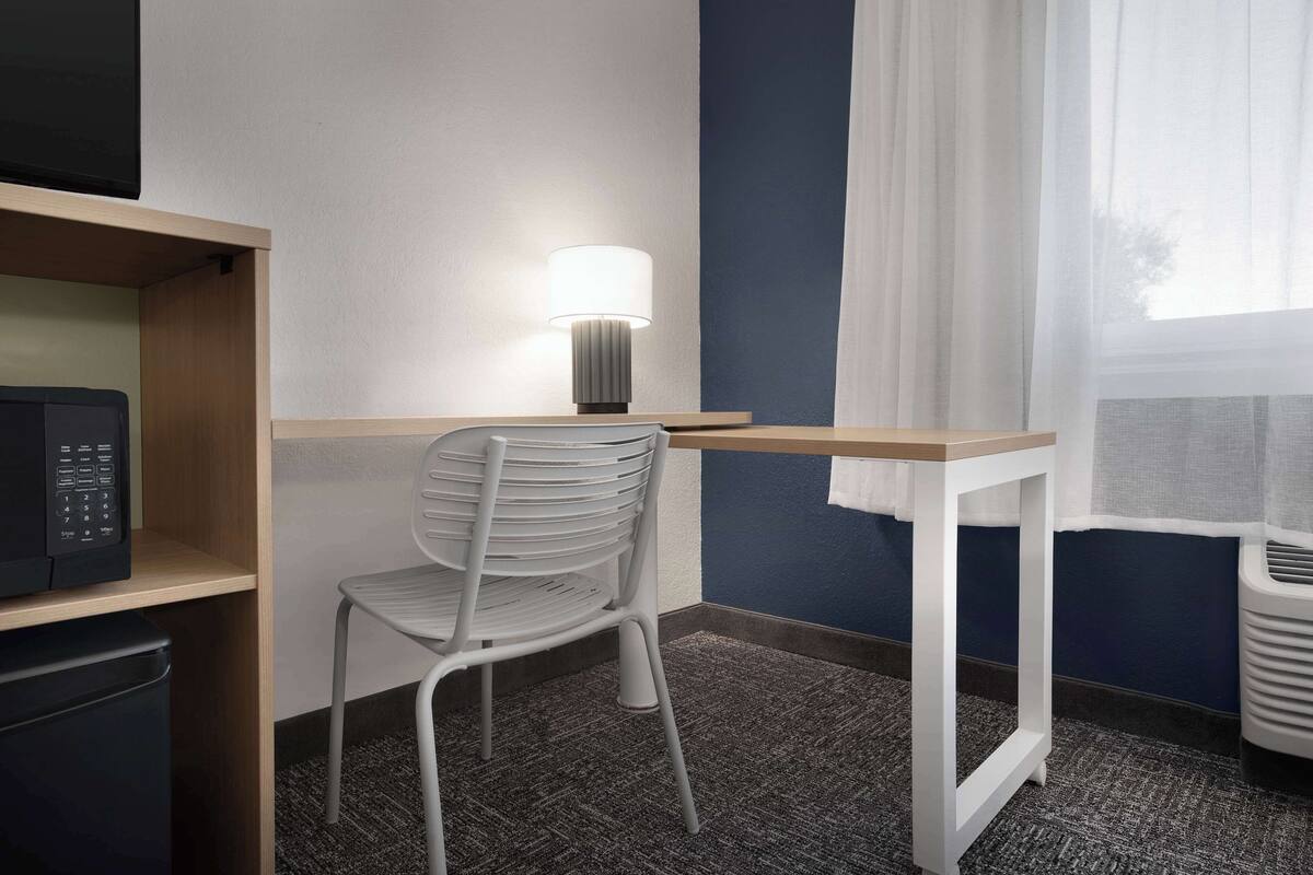 Ein Hotelzimmer mit Schreibtisch, Stuhl, Mikrowelle und einem Fenster mit Vorhängen.