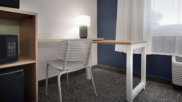Habitación de hotel con escritorio, silla, microondas y ventana con cortinas.