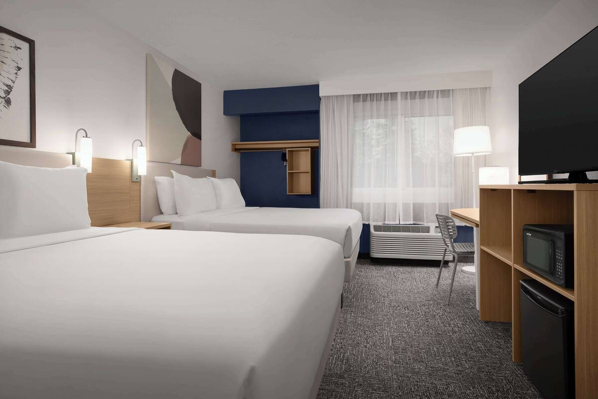 Ein Hotelzimmer mit zwei Betten, einem Schreibtisch mit Stuhl, einem Fernseher und einer Mikrowelle.
