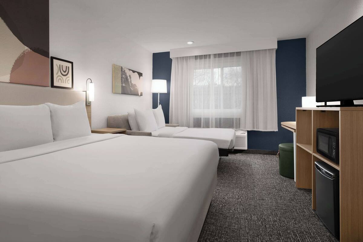Ein Hotelzimmer mit zwei Betten, einem Flachbildfernseher, einer Mikrowelle und einer kleinen Küchenzeile.