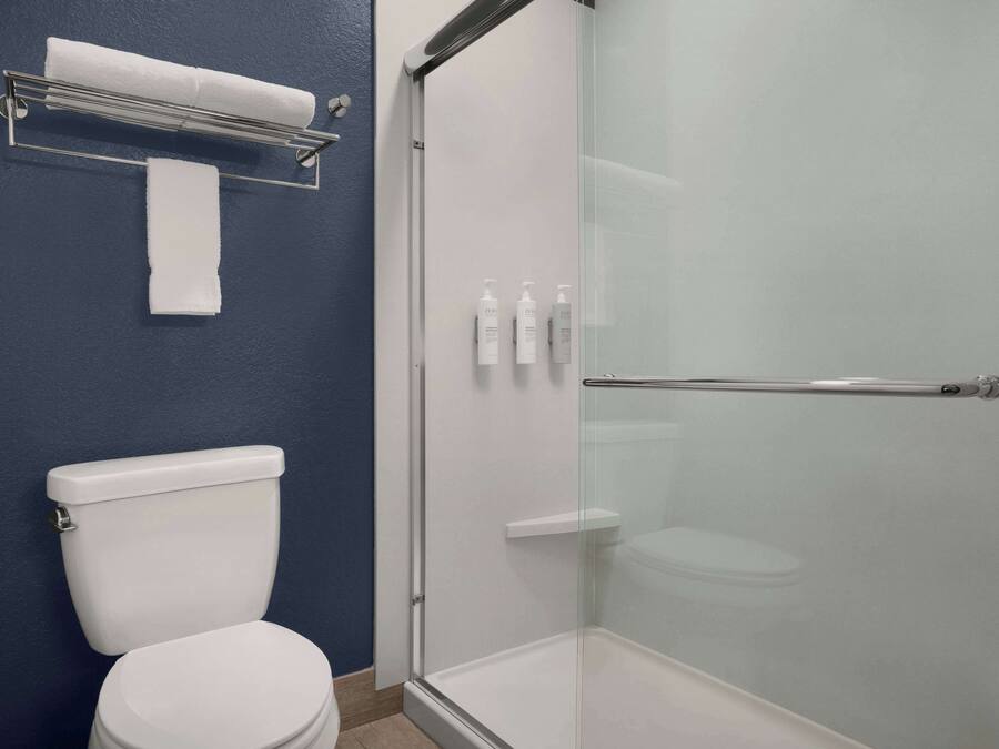 Un baño con inodoro blanco, ducha con mampara de vidrio y toallero con una toalla.