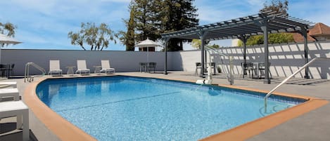 Una piscina con sillas de descanso y una pérgola.