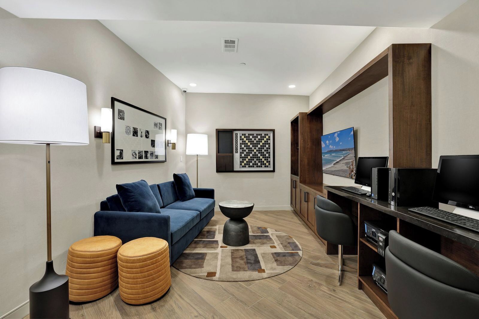 A modern living room with a sofa, ottomans, a coffee table, a desk with computers, and artwork on the walls.