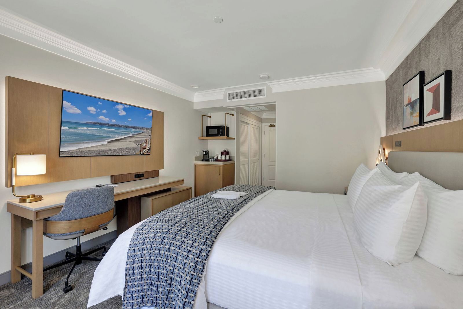 Una camera d'albergo con un letto, una scrivania, una sedia, una televisione e vista sulla spiaggia.