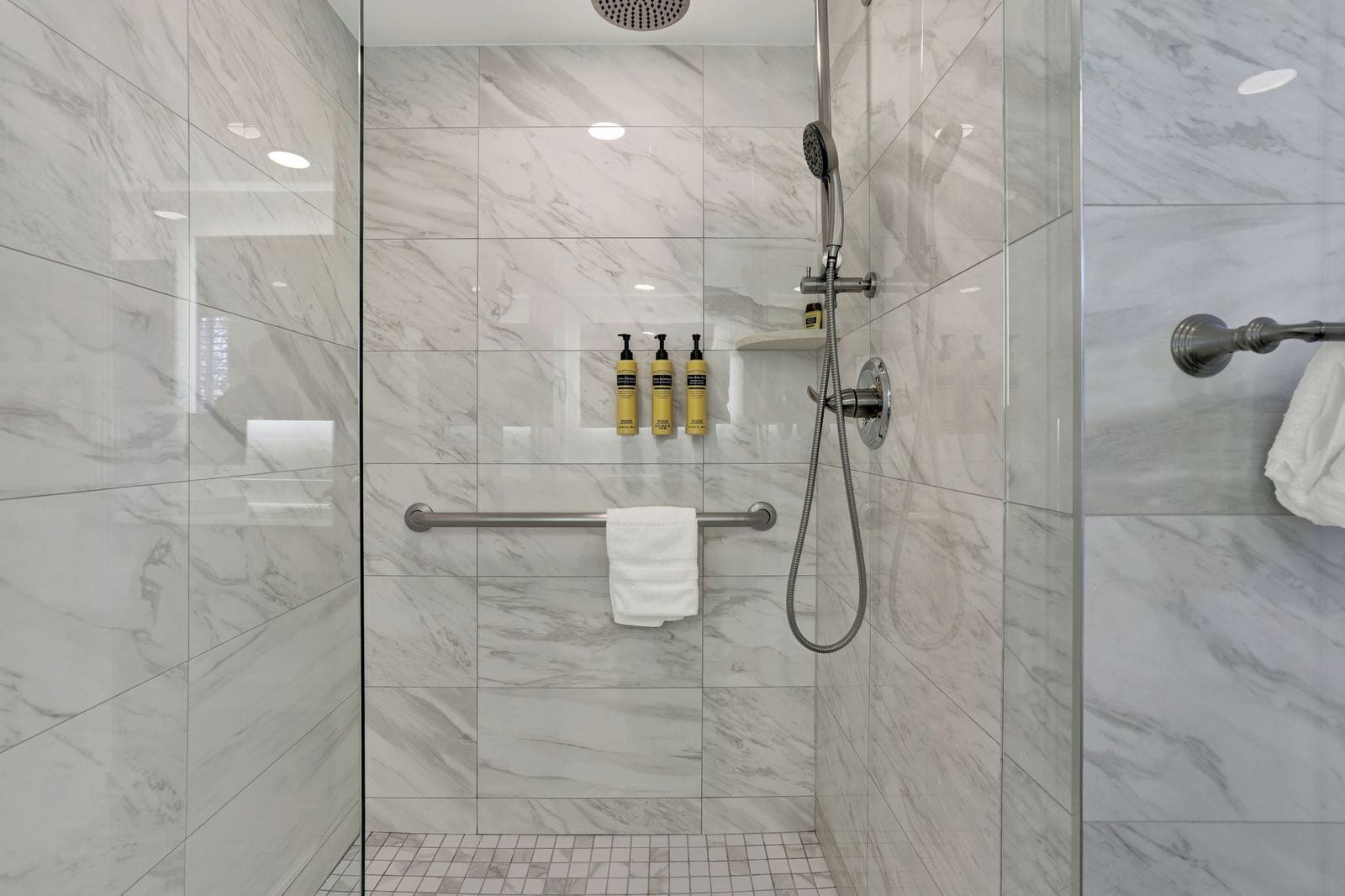 A modern shower with a handheld showerhead, a towel rack, and two bottles of shampoo and conditioner.