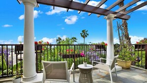 A covered outdoor area with two white chairs, a round table, and a potted plant.