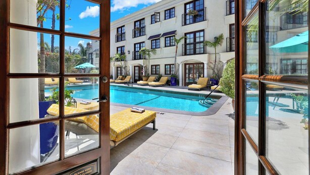 A poolside view with a clear sky, a pool, lounge chairs, and a building with multiple windows and balconies.