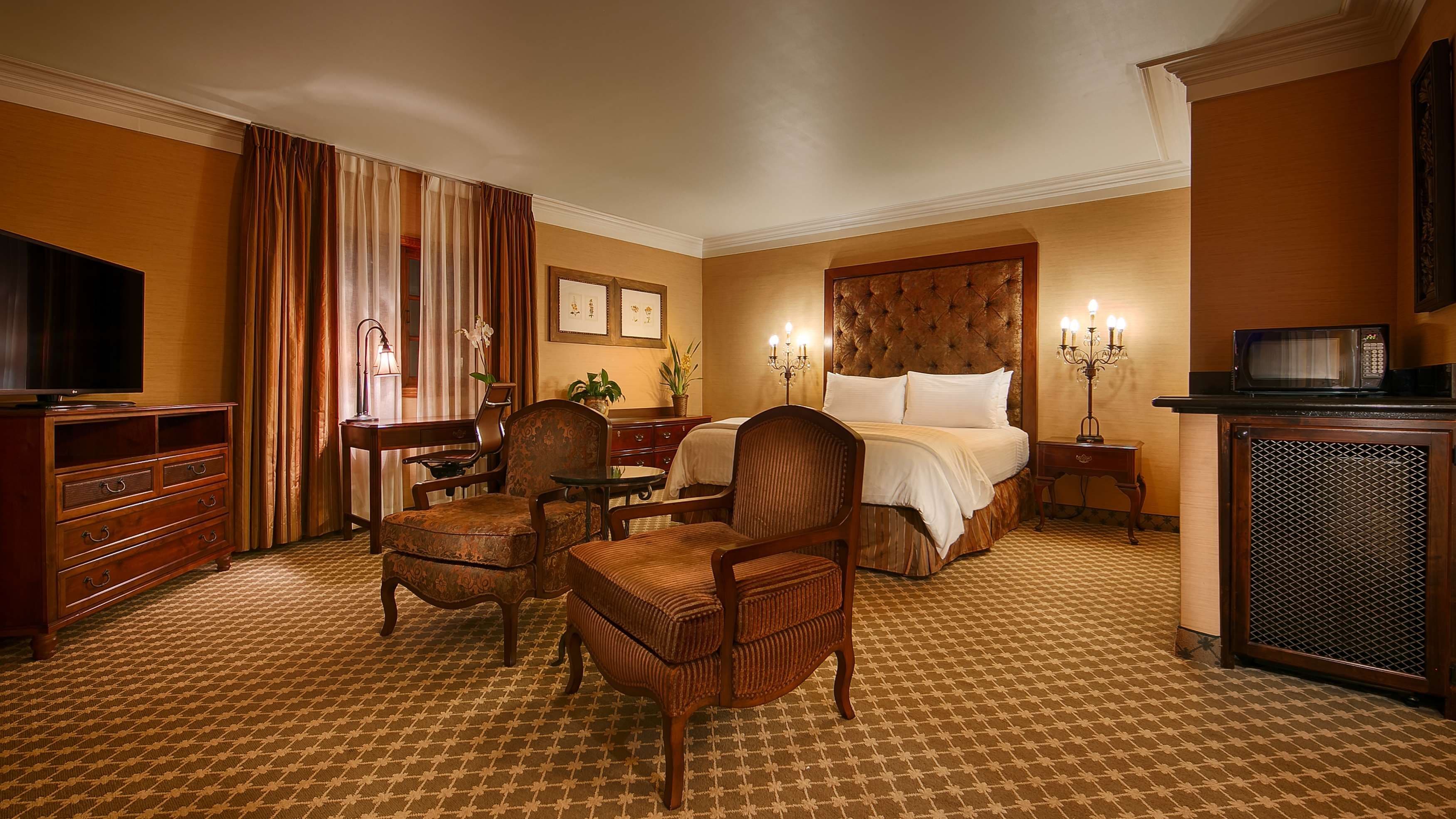 A hotel room with a bed, a desk, a television, a chair, and a microwave.