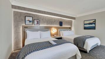 A hotel room with two beds, a headboard with built-in lighting, a small bedside table with a phone, and a wall-mounted artwork.