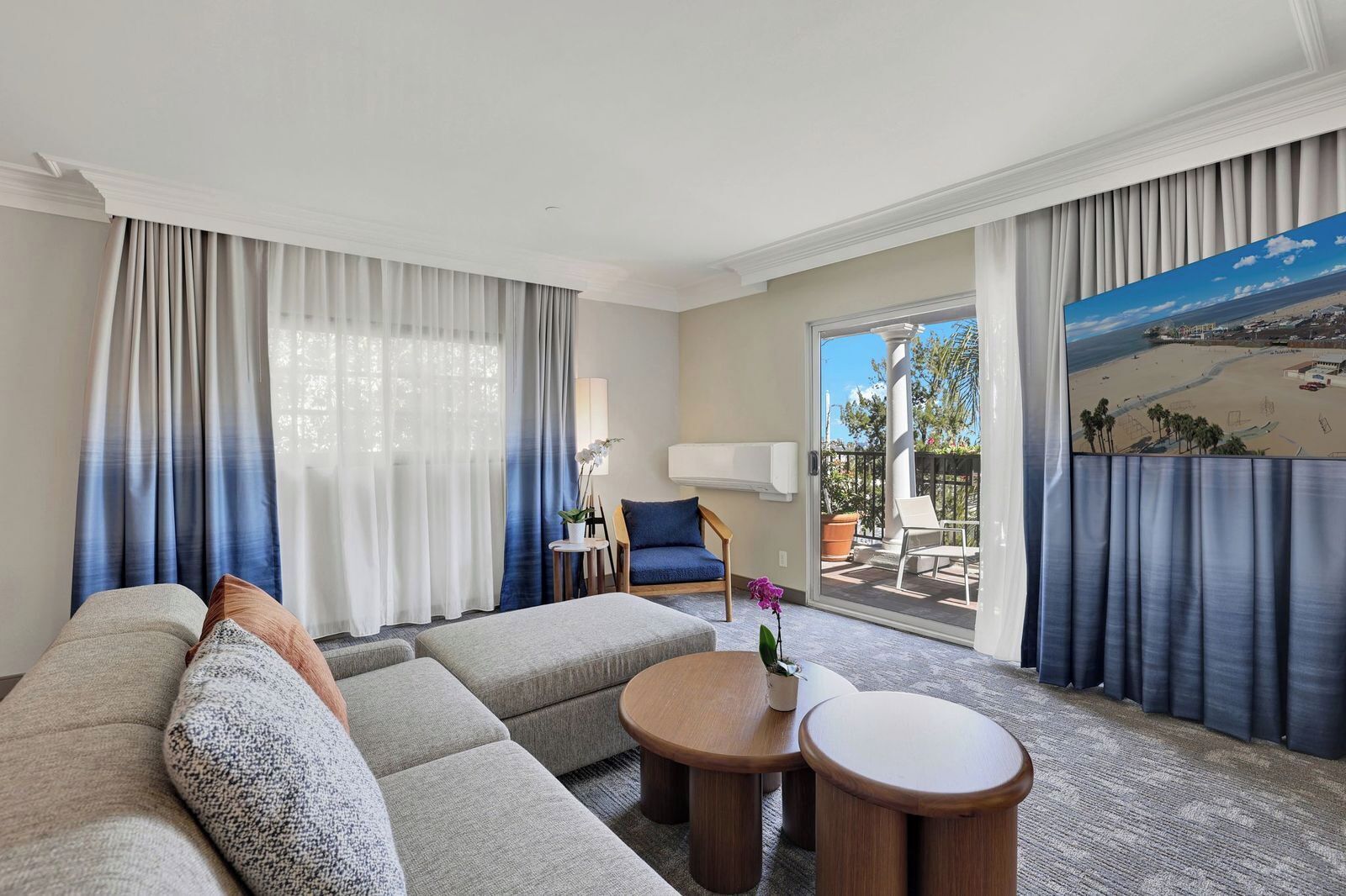 Habitación de hotel moderna con un sofá grande, una mesita, una silla y un balcón con vistas.